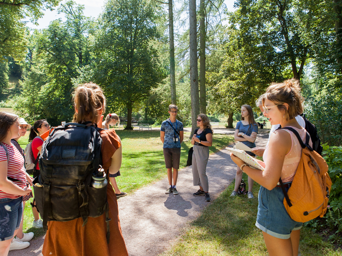 Gruppe junger Schüler*innen steht im Kreis aufgestellt im Park Tiefurt