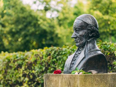 Eine dunkel gehaltene Büste von Wieland, vor die eine rote Blume glegt wurde