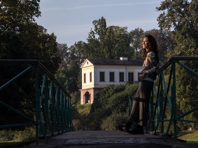 Eine Frau steht auf einer Brücke, im Hintergrund erkennt man ein Gebäude in antikem Stil