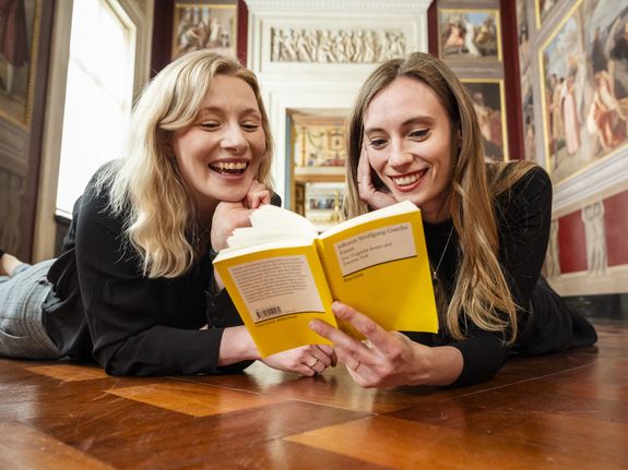 Zwei Personen liegen auf den Holzfußboden und lesen ein Buch