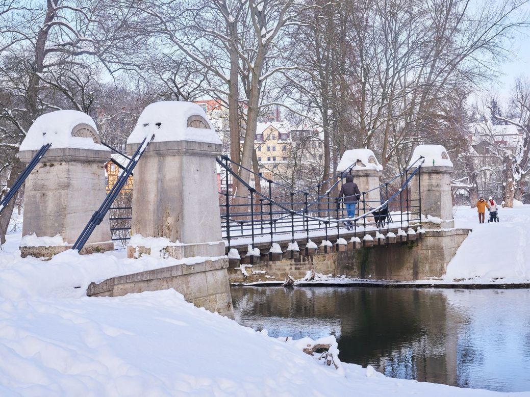 Eingeschneite Hängebrücke mit Fluss im Park an der Ilm.