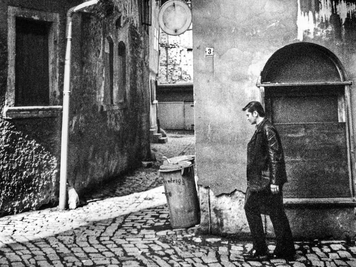 Schwarz-Weiß-Fotografie vor einer Gasse zwischen zwei Gebäuden, an der ein Mann vorbeigeht