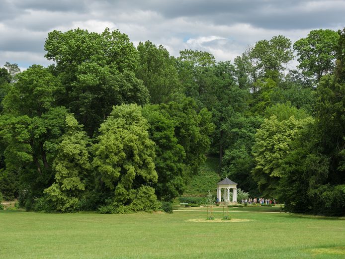 Eine Besuchergruppe betrachtet den Musentempel im Park.