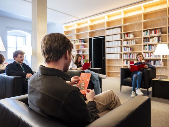 Mehrere Personen lesen entspannt in Sesseln in einer gemütlichen, hellen Sitzecke in der Bibliothek.