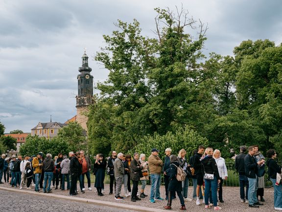 Eine Schlange von Menschen steht vor einer Parkanlage.
