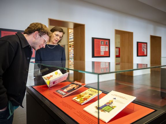 Zwei Personen sehen sich in einer Vitrine Mephisto-Illustrationen in Büchern an.