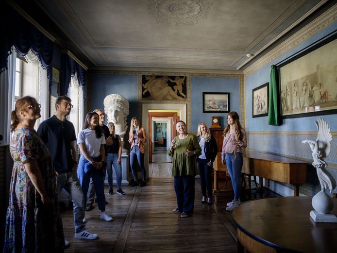 Dans une pièce bleue avec vue à travers un alignement de portes, plusieurs personnes se tiennent autour d'un guide et écoutent leurs explications.