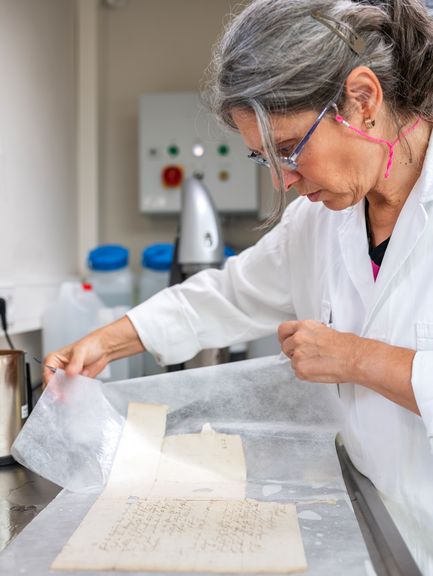 Eine Restauratorin arbeitet an einer beschädigten Handschrift.