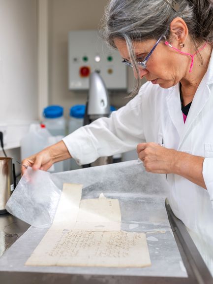 Eine Restauratorin arbeitet an einer beschädigten Handschrift.