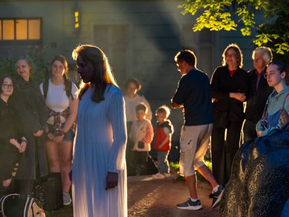 Menschen schauen auf eine blonde Frau in einem weißen Kleid.