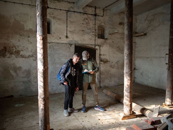 Zwei Schüler in einem baufälligen Gebäude. Sie schreiben etwas auf ein Klemmbrett.