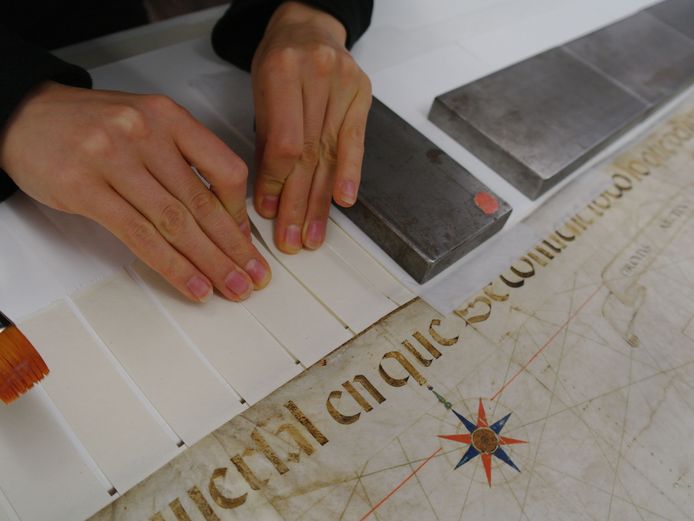 Die Fotografie zeigt, wie die beiden großformatigen Ribeiro-Weltkarten aus Pergament von 1527 und 1529 in Passepartouts aus Wabenplatten neu montiert werden. Das gelingt mit Hilfe von Fälzen aus Japanpapier und unter Verwendung von Weizenstärkekleister. Signaturen: KT 020-57S und KT 020-58S.