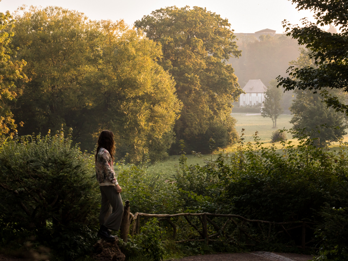 Eine Frau blickt mit dem Rücken zur Kamera über die Wiesen des Parks an der Ilm und richtet den Blick auf ein Gartenhaus