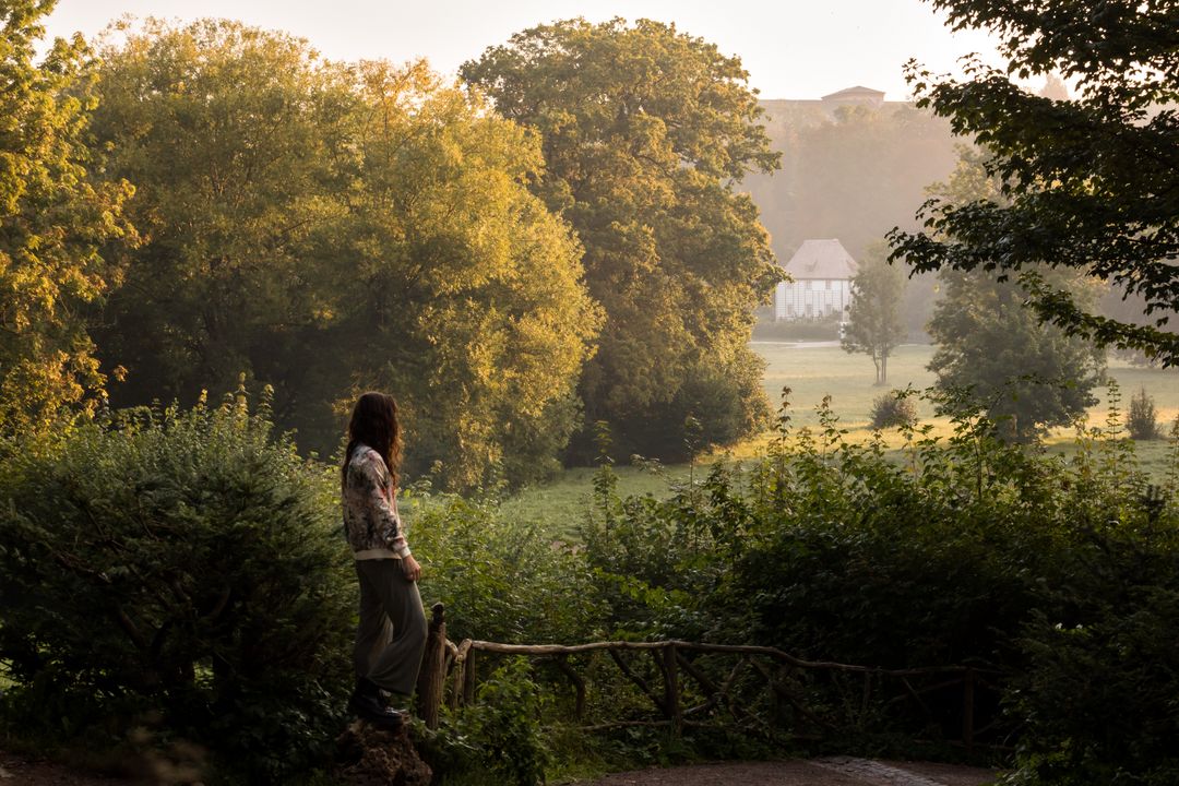 Eine Frau blickt mit dem Rücken zur Kamera über die Wiesen des Parks an der Ilm und richtet den Blick auf ein Gartenhaus