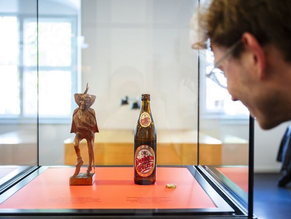 Besucher betrachtet eine Vitrine mit einer Mephisto-Figur und einer Bierflasche mit Mephisto-Etikett.