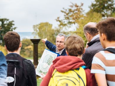 Guide einer Schülergruppe zeigt auf die Schlossfontäne im Park Belvedere