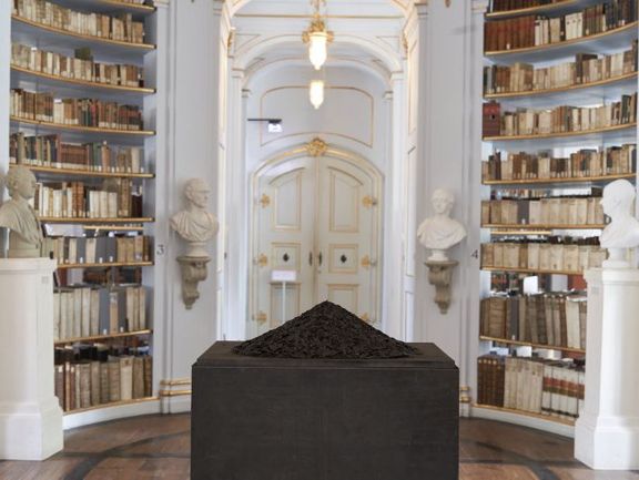 Inmitten des hellen Rokokosaals der Herzogin Anna Amalia Bibliothek ist auf einem schwarzen Sockel Asche in Form eines Vulkankegels aufgehäuft. 