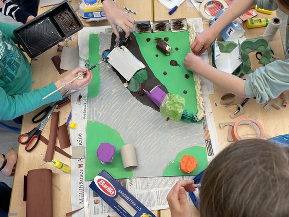 An einem Tisch basteln vier Kinder ein Modell