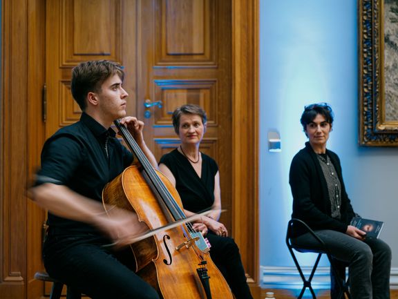 Zwei Personen schauen auf eine Person, die Cello spielt.