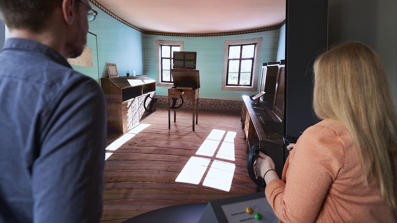 Zwei Personen von Hinten stehen vor einem großen Screen und steuern mit Controllern in der Hand den Goethe-Apparat.