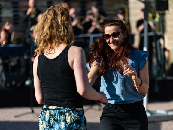 Zwei Frauen tanzen fröhlich miteinander zu Live-Musik vor dem Co-Labor. 