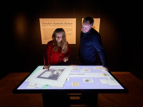 Zwei Menschen stehen vor einem digitalen Tisch und bewegen Objekte