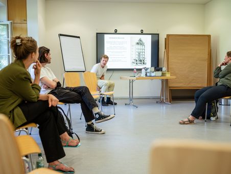 Tagungsteilnehmende sitzen im Stuhlkreis und hören einer Präsentation zu.