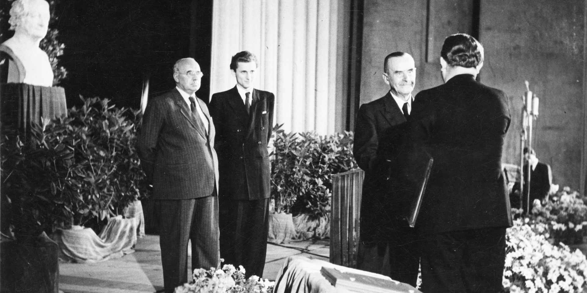 Schwarz-weiß Bild mit drei Männern in Anzügen in einem Raum