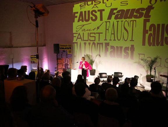 Eine Frau steht vor Publikum und soricht in ein Mikrofon.